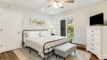 A bedroom with a bed, a ceiling fan, a TV, a dresser, and a window.