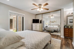 Une chambre à coucher comprenant un lit, un ventilateur de plafond, une commode, un téléviseur et un grand miroir.