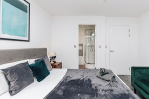 Relax in a stylish room with a neatly made bed, a green chair, and a unique abstract painting.