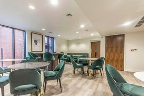 Enjoy dining in comfort with round tables and individual chairs, surrounded by natural light and well-illuminated by ceiling-mounted fixtures.