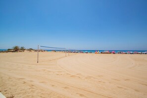 Une plage avec un filet de volley-ball, des palmiers et des parasols.