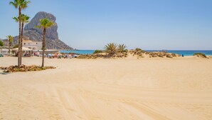 A sandy beach with palm trees, a rocky mountain, and a clear blue sky.