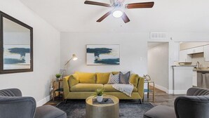 Una sala de estar con un sofá amarillo, una mesa de centro redonda y un ventilador de techo.