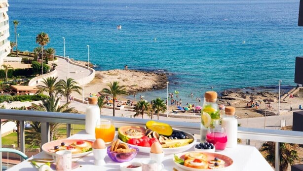 A balcony with a breakfast table overlooking a beach with a clear view of the ocean and a rocky shoreline. - Apartment 'Playa Salinas Grupo Terra De Mar' with Sea View, Wi-Fi and Air Conditioning (Calpe)
