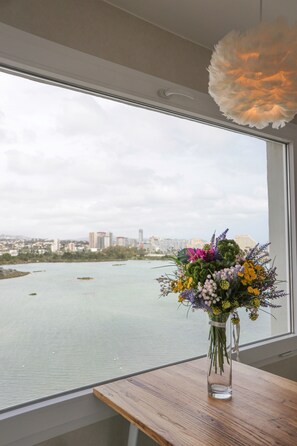 Vista de la ciudad a través de una ventana, con un florero sobre una mesa de madera.