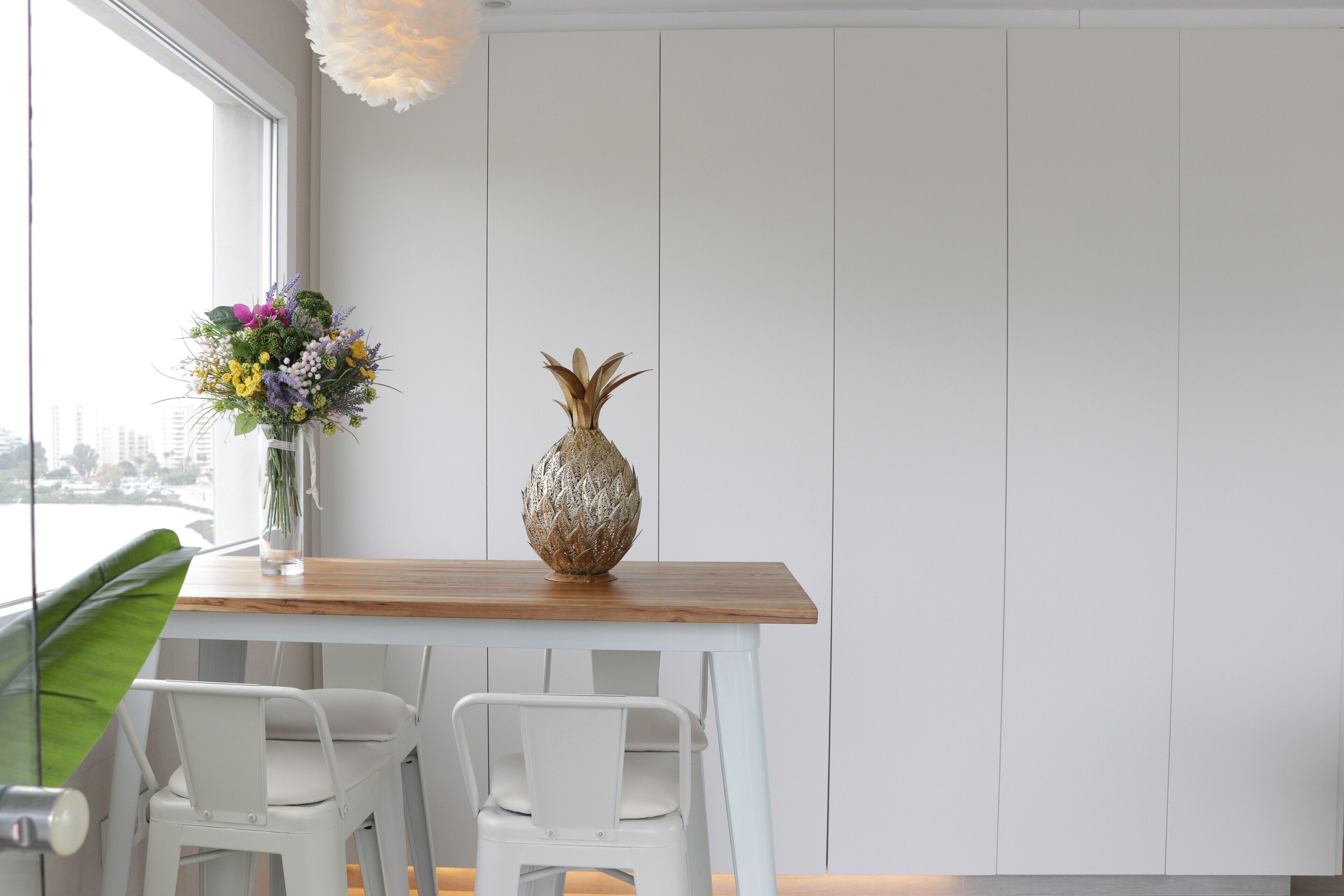 A dining area with a wooden table, white chairs, a vase with flowers, and a decorative vase.