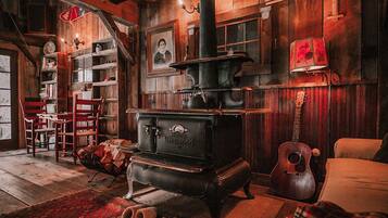 A rustic room with a large wood-burning stove, wooden walls, a guitar, and a plaid blanket on the floor.