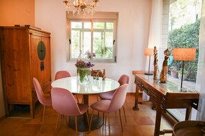 Un coin repas avec une table ronde, des chaises roses, un buffet en bois et une fenêtre donnant sur un paysage verdoyant.