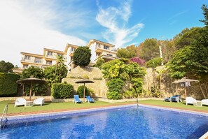 A swimming pool with lounge chairs, a stone wall, and a multi-story building in the background. - Bungalow 'Alegre Playa Grupo Terra De Mar' with Mountain View, Wi-Fi and Air Conditioning (Calpe)