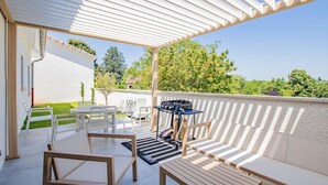 Un patio al aire libre cubierto con mesa y sillas, una parrilla y vistas al follaje circundante.
