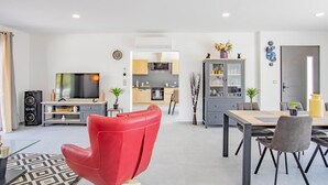 Una sala moderna con una butaca roja, un televisor y una zona de comedor con mesa y sillas.