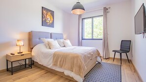 Un dormitorio con cama, mesita de noche, lámpara y un cuadro en la pared.