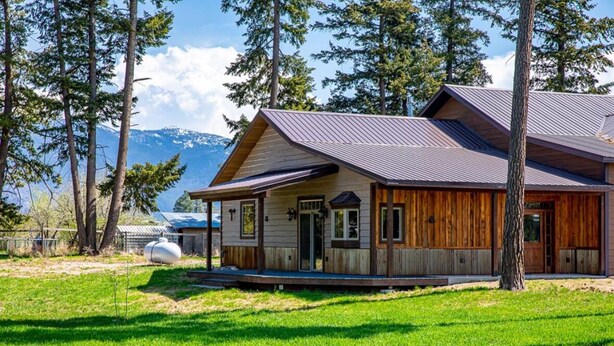 Eine Holzhütte mit Metallbedachung, umgeben von Bäumen und einer Rasenfläche.