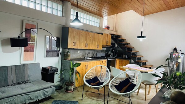 A modern kitchen with wooden cabinets, a dining area with white chairs, and a grey sofa.