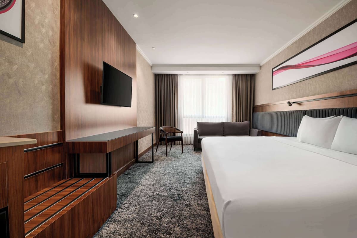 Une chambre d’hôtel avec un grand lit, un bureau avec une chaise, un téléviseur fixé au mur et une fenêtre avec des rideaux.