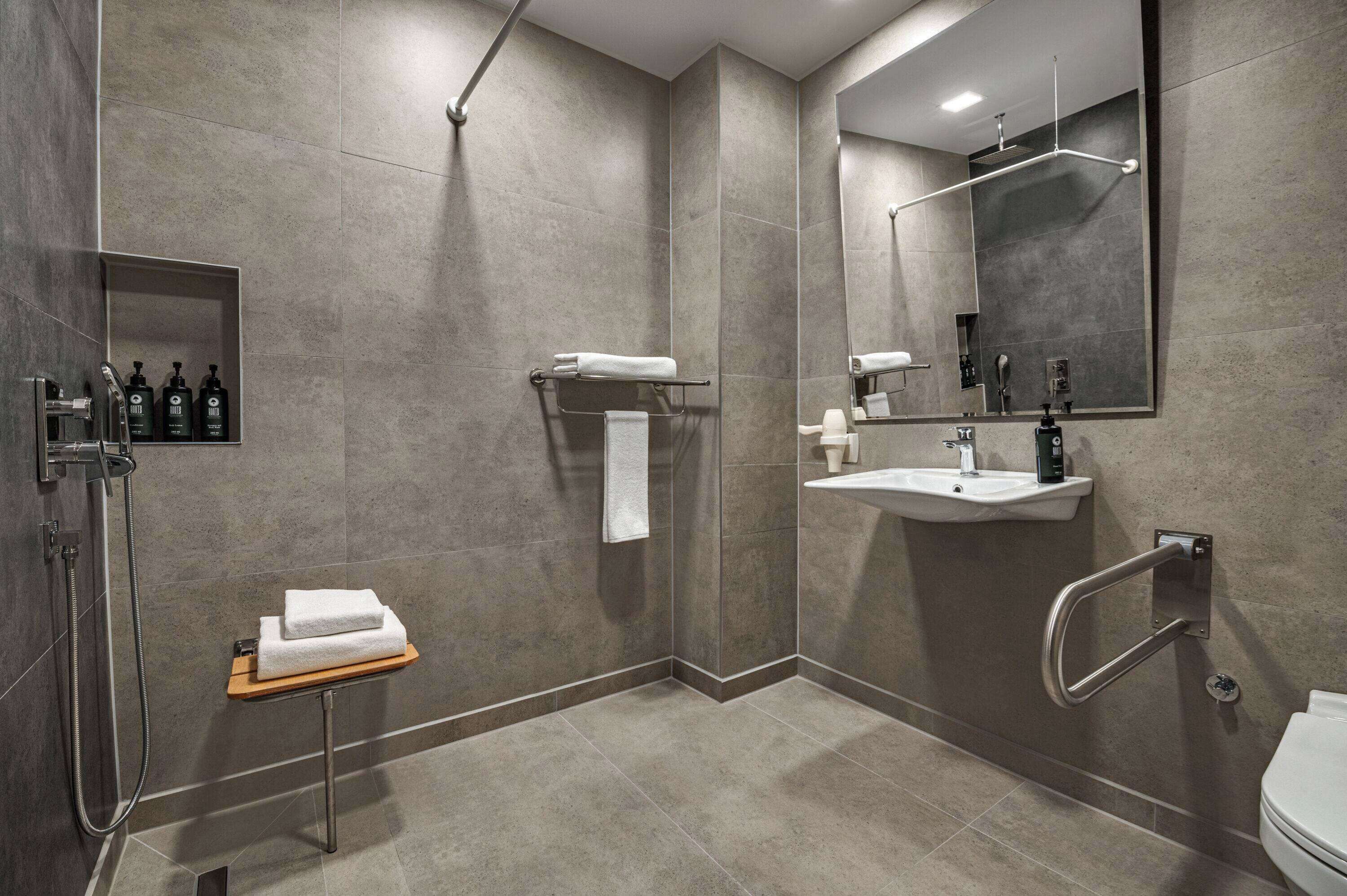 Une salle de bain moderne équipée d’une douche, d’un lavabo et de toilettes. On y trouve un porte-serviettes, une étagère avec des articles de toilette et un miroir.