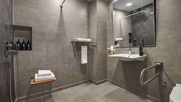 Une salle de bain moderne équipée d’une douche, d’un lavabo et de toilettes. On y trouve un porte-serviettes, une étagère avec des articles de toilette et un miroir.