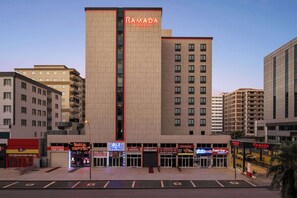 Een meerhoog hotel met een opvallend ‘RAMADA’ bord, met een modern architectonisch ontwerp en een centrale verticale strook.