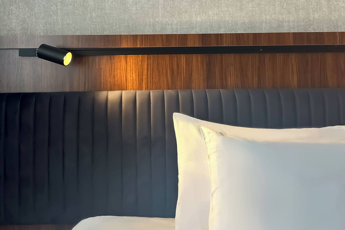 Une chambre d’hôtel moderne avec une tête de lit en bois, un grand tableau abstrait et un lit parfaitement fait avec du linge de maison blanc.