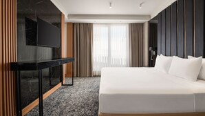 Ein modernes Hotelzimmer mit einem großen Bett, einem flachbildfernseher an einer Marmorkonsole und einem großen Fenster mit Vorhängen.