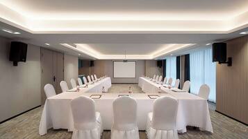 A conference room with a long table, white chairs, and a projector screen.