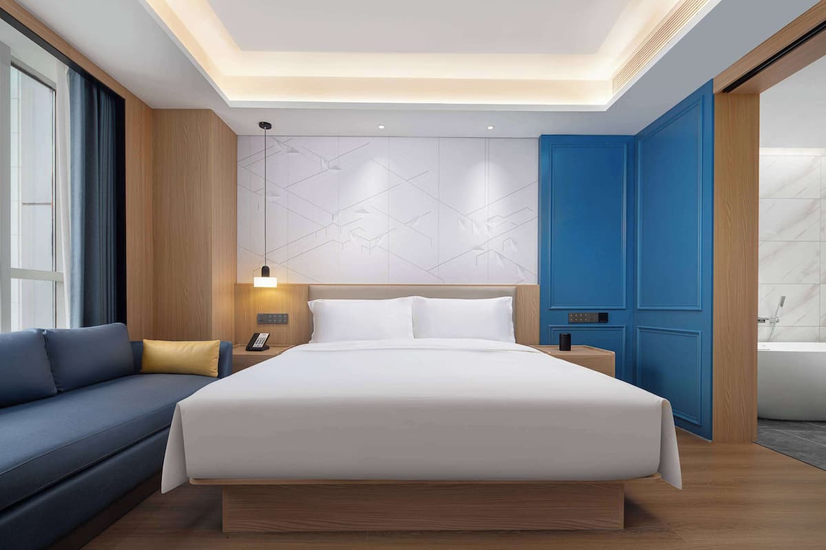 Ein modernes Hotelzimmer mit einem großen Bett, einer Couch, einem Nachttisch mit Lampe und einem Badezimmer mit Badewanne.