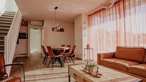A modern living room with a sofa, a dining table with chairs, a coffee table, and a staircase leading to an upper floor. - Modern Waterfront Retreat (Uitgeest)