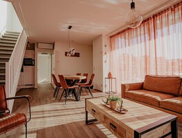 A modern living room with a sofa, a dining table with chairs, a coffee table, and a staircase leading to an upper floor.