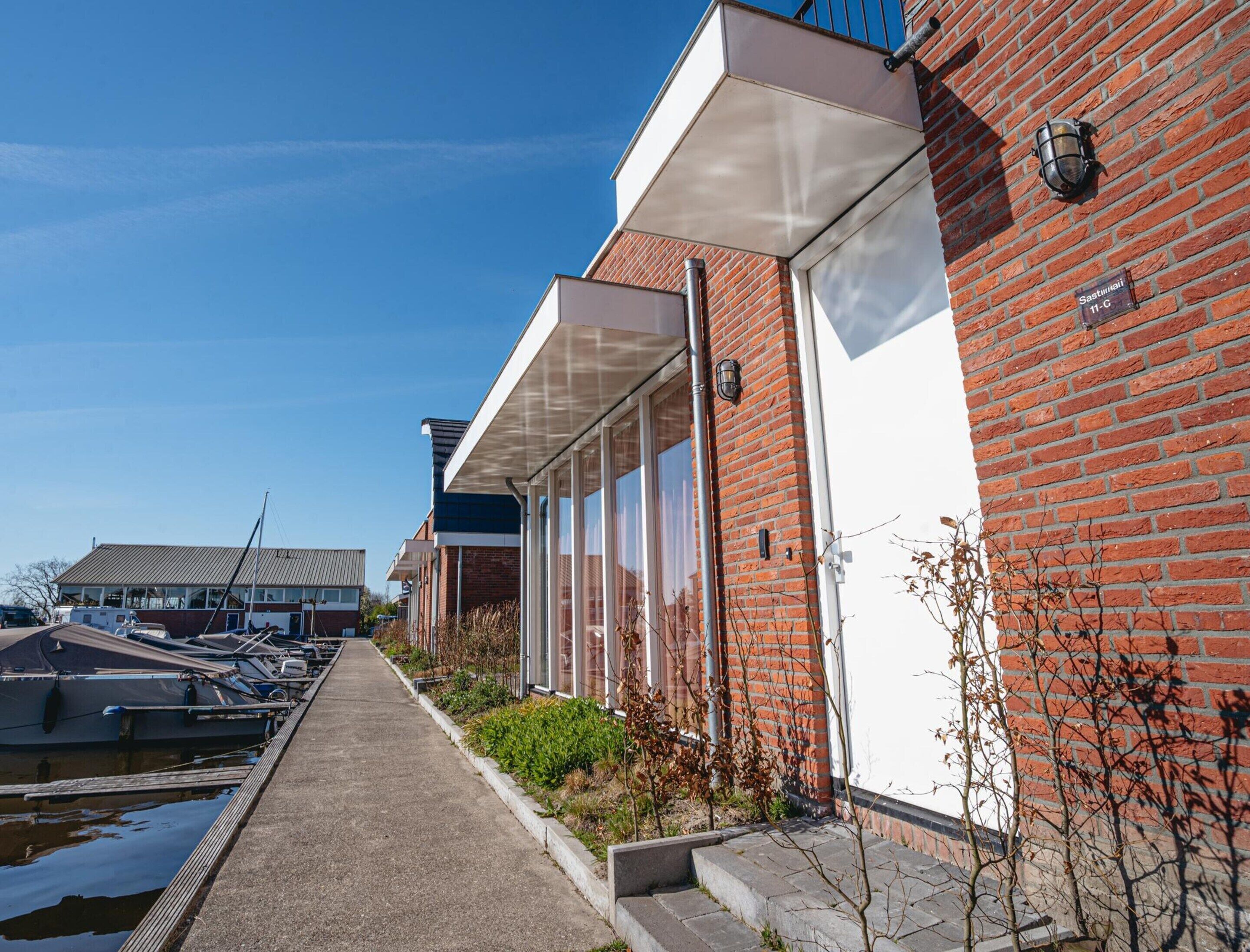 A modern building with large windows and a brick facade, adjacent to a marina with boats docked.