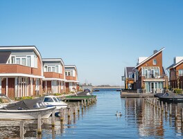 A canal lined with modern houses, boats docked along the water, and a clear blue sky.