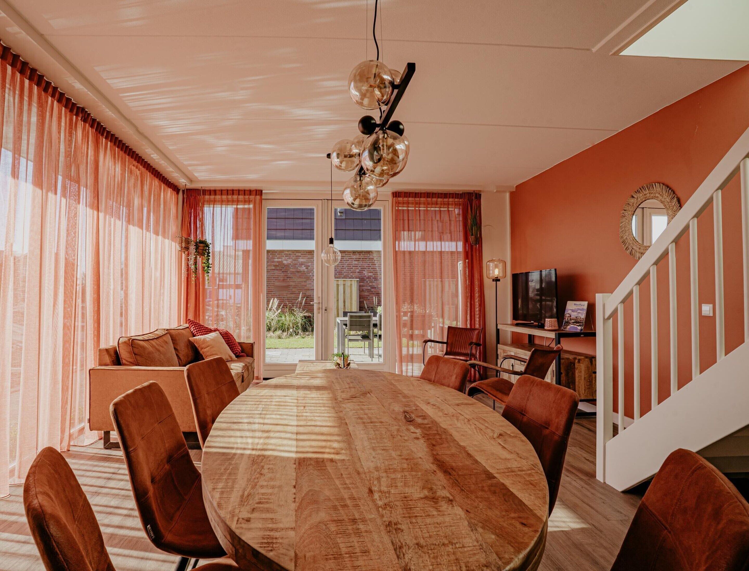 Ein großzügiger Essbereich mit einem großen Holztisch, modernen Stühlen, einem Fernseher und einer Treppe mit einem dekorativen Spiegel.