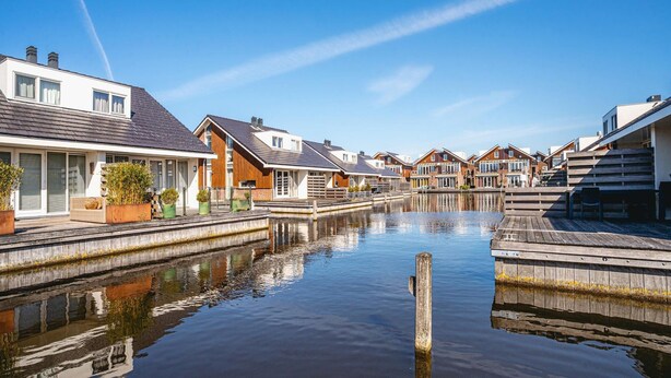 A canal-side residential area with houses, a wooden dock, and calm water. - Modern Waterfront Retreat (Uitgeest)