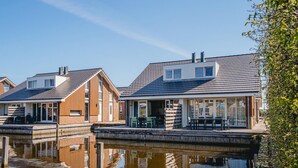A row of modern houses with a dock extending into a calm body of water, reflecting the buildings. - Modern Waterfront Retreat (Uitgeest)