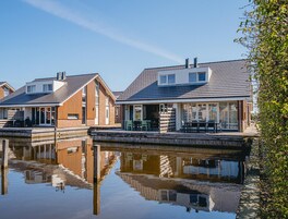 A row of modern houses with a dock extending into a calm body of water, reflecting the buildings.