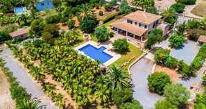 Eine Luftaufnahme eines Anwesens mit Swimmingpool, umgeben von üppiger Vegetation, einem großen Haus mit Ziegeldach und einem kleinen Nebengebäude.