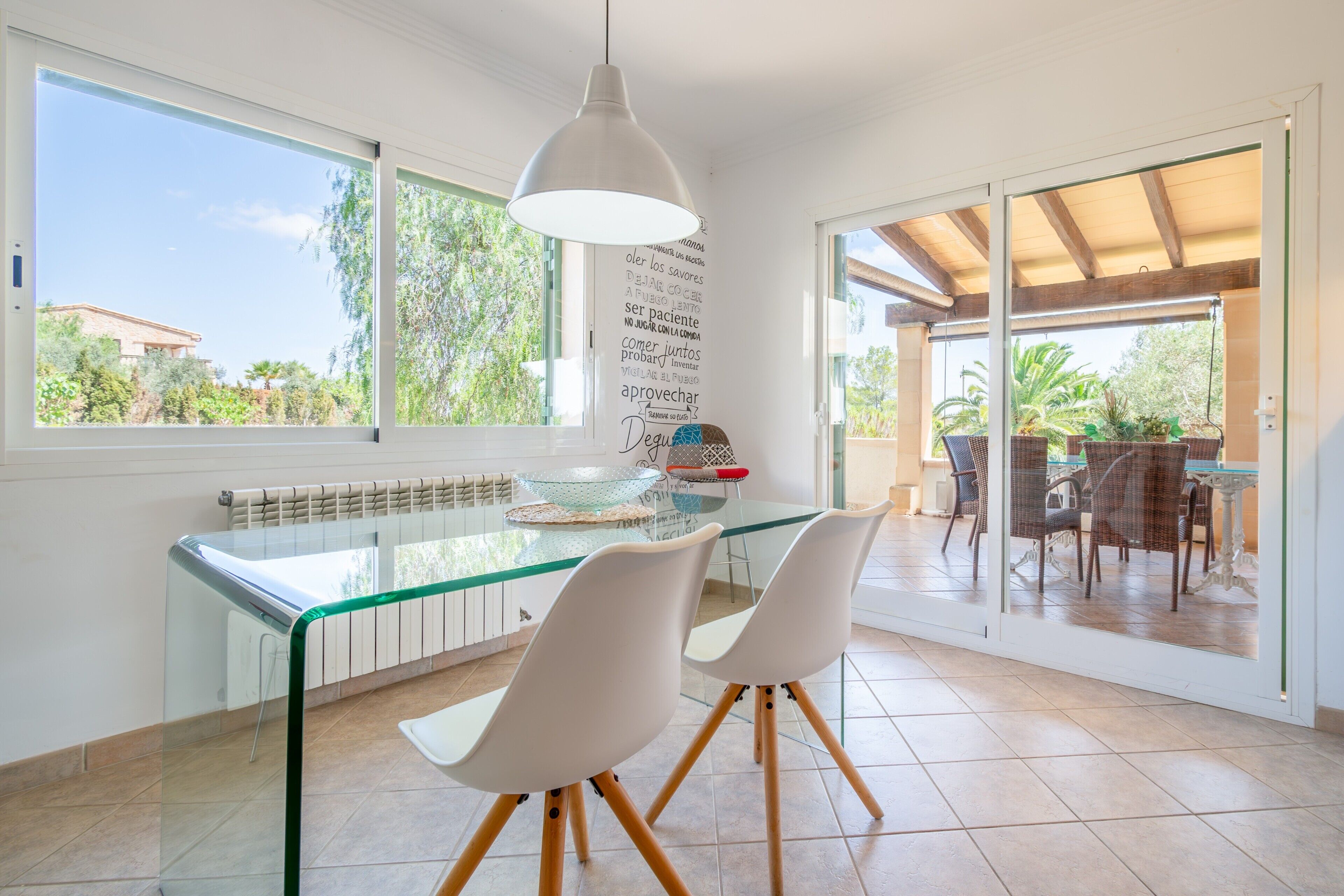A modern kitchen with a glass dining table, white chairs, and a pendant light.