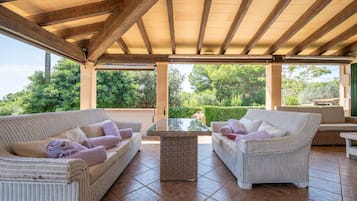 Une terrasse extérieure aménagée avec des meubles en osier, une table à plateau en verre et une vue sur la verdure.