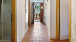 Un pasillo con suelo de baldosas, puertas de madera y vistas al exterior.
