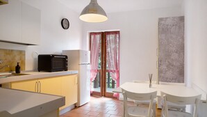 Cocina compacta con microondas, refrigerador, lavamanos y comedor con sillas y mesa.
