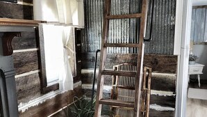 A rustic interior with a wooden ladder, a potted plant, and a window with curtains. - Southern Blooms! Porch Swinging, Pet-Friendly, Tiny Home near Kentucky Lake! (Springville)