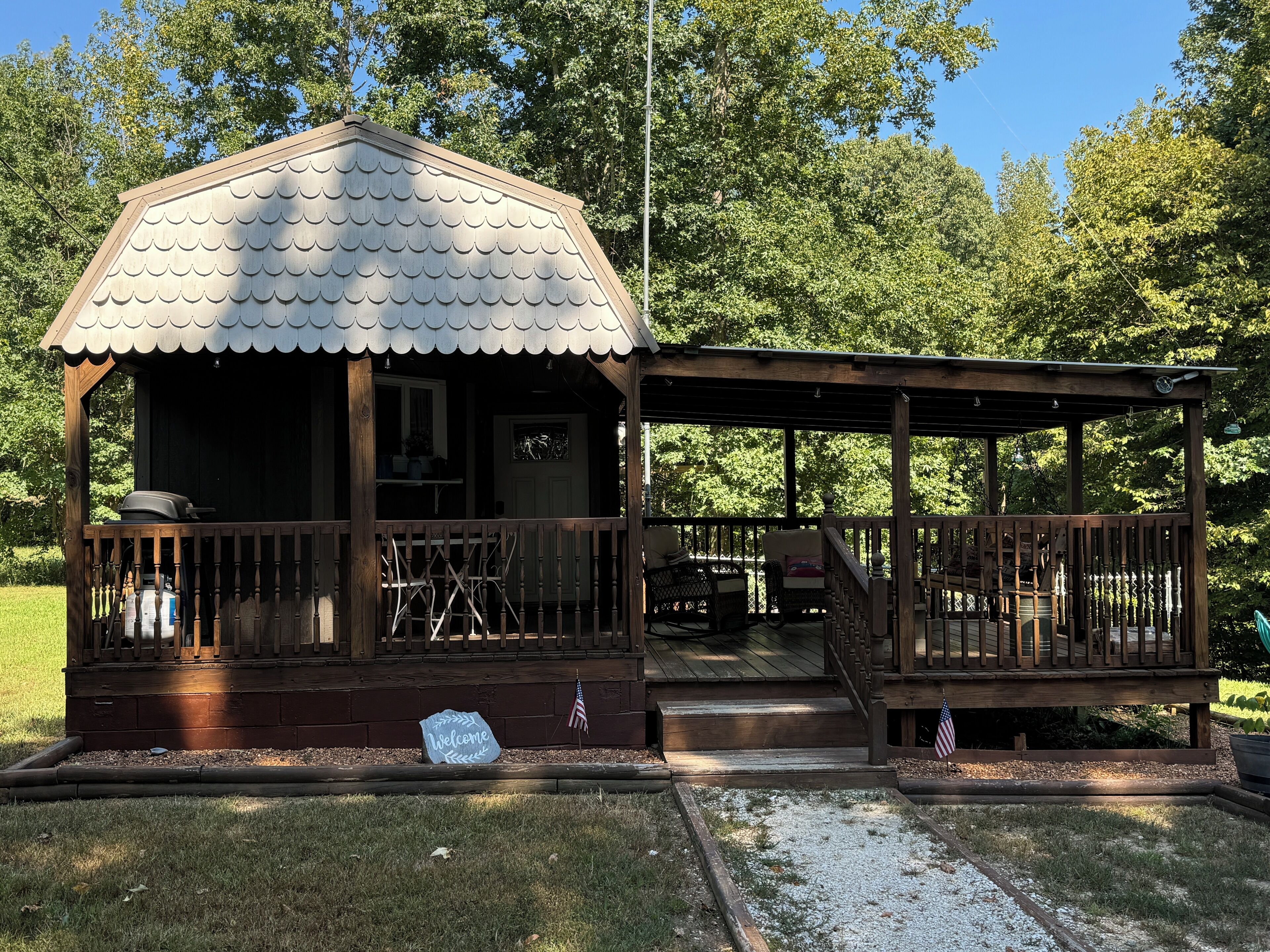 A wooden cabin with a covered porch, a welcome sign, and an American flag.