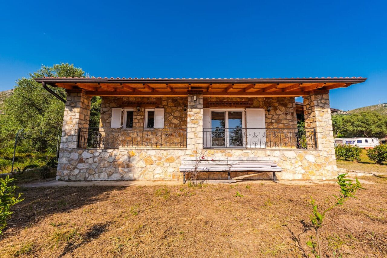 A stone house with a wooden porch, a bench, and a clear view of the surrounding landscape.
