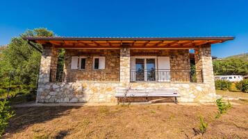 A stone house with a wooden porch, a bench, and a clear view of the surrounding landscape.