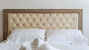 Ein Bett mit einem gepolsterten Kopfteil, weißer Bettwäsche und einem Holzrahmen.