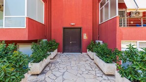 Ein rotes Gebäude mit einer zentralen Tür, Steinstufen und Pflanzgefäßen mit grünen Sträuchern.