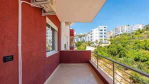 Ein Balkon mit roter Wand, einem Fenster und Blick auf andere Gebäude und Grünflächen.