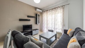Ein modernes Wohnzimmer mit einer Sofagarnitur, einem Flachbildfernseher, einem Couchtisch und einer Deckenleuchte.