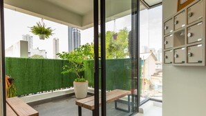 A balcony with a wooden bench, a potted plant, and a glass door leading to a city view. - Minima 8  (George Town)