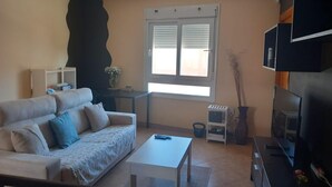 Ein Wohnzimmer mit einer Couch, einem Couchtisch, einem Fernseher und einem Fenster mit Jalousien.