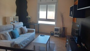 Ein Wohnzimmer mit Sofa, Couchtisch, Fernseher und einem Fenster mit Jalousien.